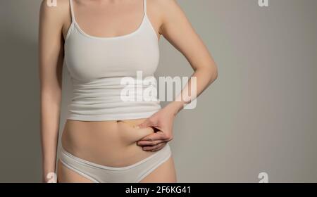 Skinny Fat stellte eine unkenntliche Frau vor, die ihr Bauchfett kneifen würde. Frau`s Figur Nahaufnahme RAW Studio in grauem Hintergrund aufgenommen. Diät und Fettabbau concep Stockfoto